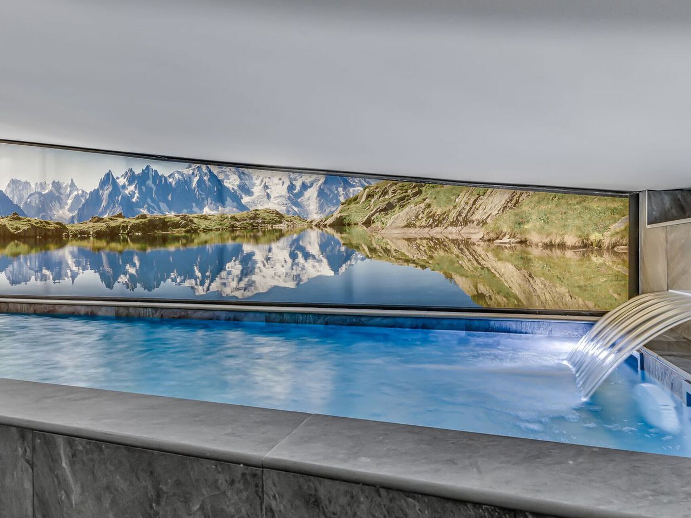 A pool with a mountain landscape mural, a clear blue pool, and a waterfall feature.