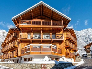 A multi-story wooden chalet with balconies, a stone foundation, and a sign indicating it is an entrance parking area. - Cozy apartment in Champagny - 8 pers, 3 bdr, Wifi (Champagny-en-Vanoise)