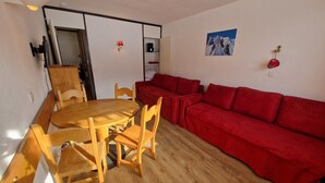 A room with a wooden dining table, chairs, a red sofa, and a small wall-mounted shelf. - Bright studio with balcony, ski-in/ski-out, sleeps 4 (La Plagne)