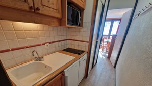 A compact kitchen with a sink, wooden cabinets, and a microwave. - Bright studio with balcony, ski-in/ski-out, sleeps 4 (La Plagne)