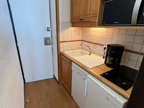 Une cuisine compacte équipée d’un évier, d’une machine à café, de meubles de rangement en bois et d’un lave-vaisselle.