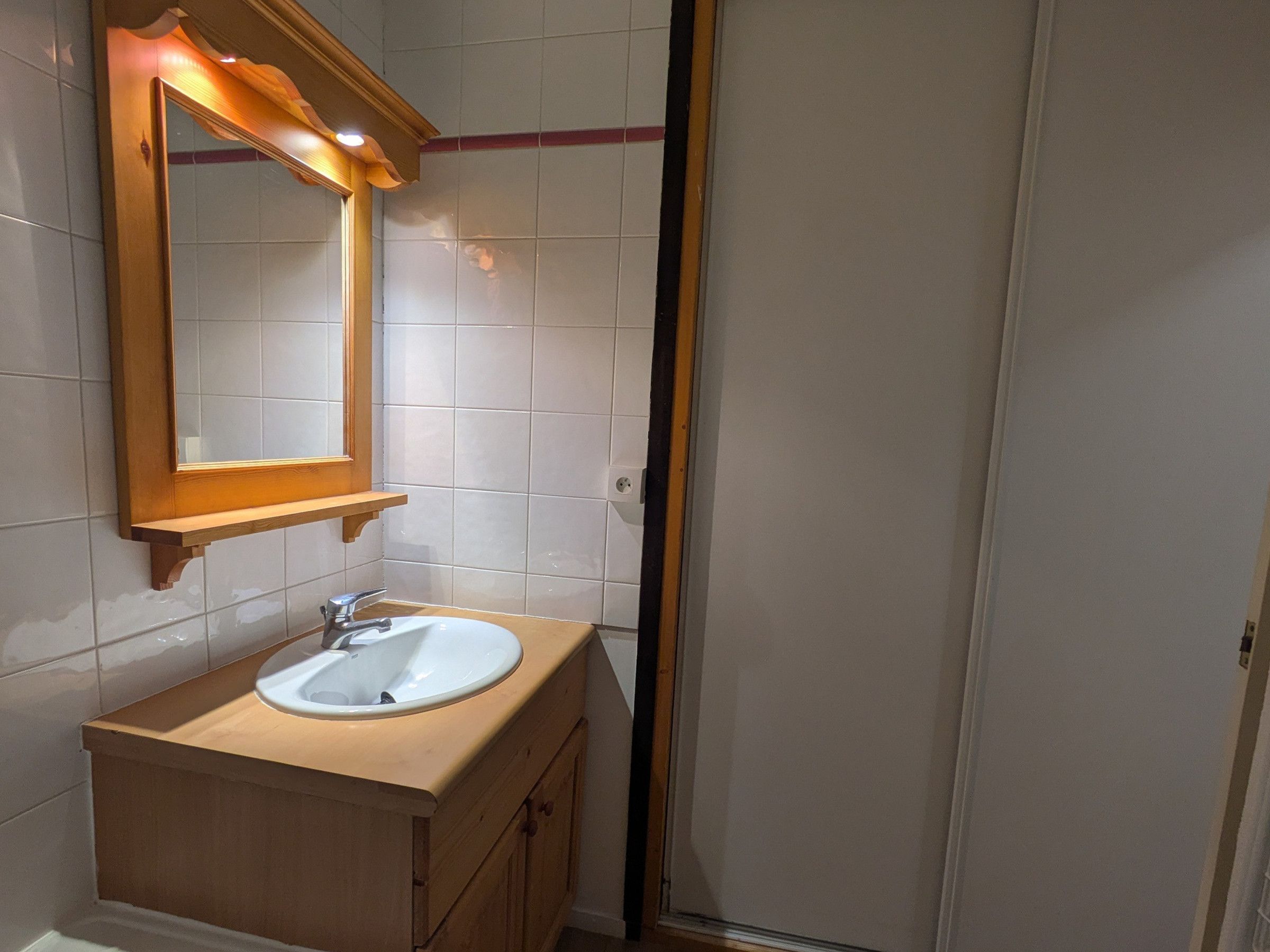 Ein Badezimmer mit einem weißen Waschbecken, einer Holz-Waschkommode und einem Spiegel mit Holzrahmen.