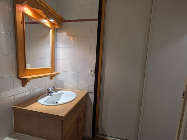 Een badkamer met een wit wastafelblad, een houten opbergmeubel en een spiegel met houten lijst.