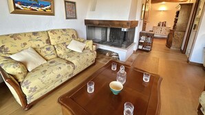 A living room with a sofa, a coffee table with glasses and a bowl, a fireplace, and a hallway leading to a kitchen.