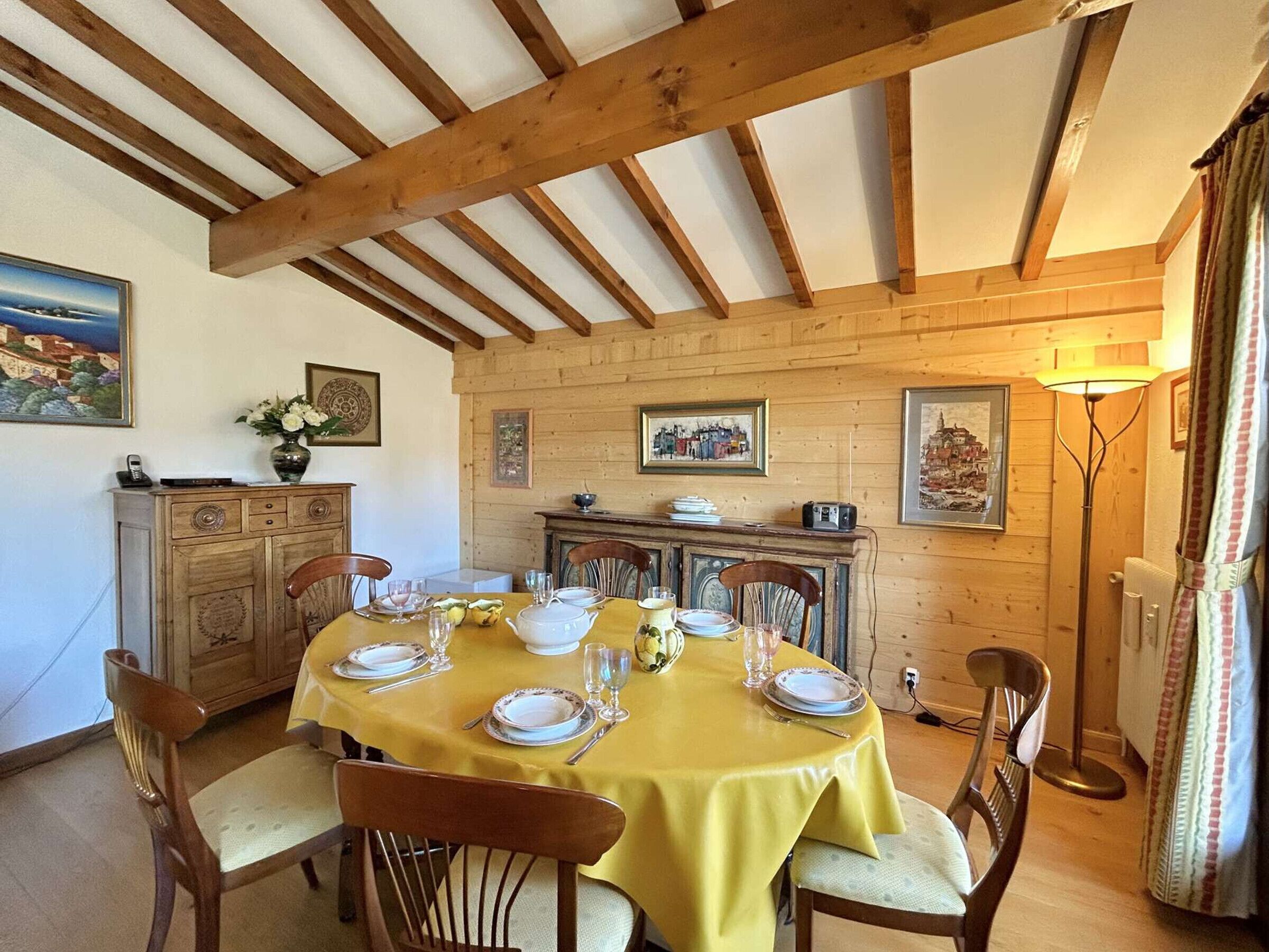 Un comedor con techo de madera, mantel amarillo y sillas de madera.