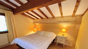 A bedroom with a wooden ceiling, a bed with white bedding, two bedside lamps, and a nightstand.