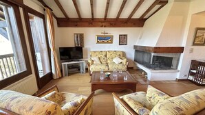 A living room with wooden beams, a sofa set, a television, and a fireplace.