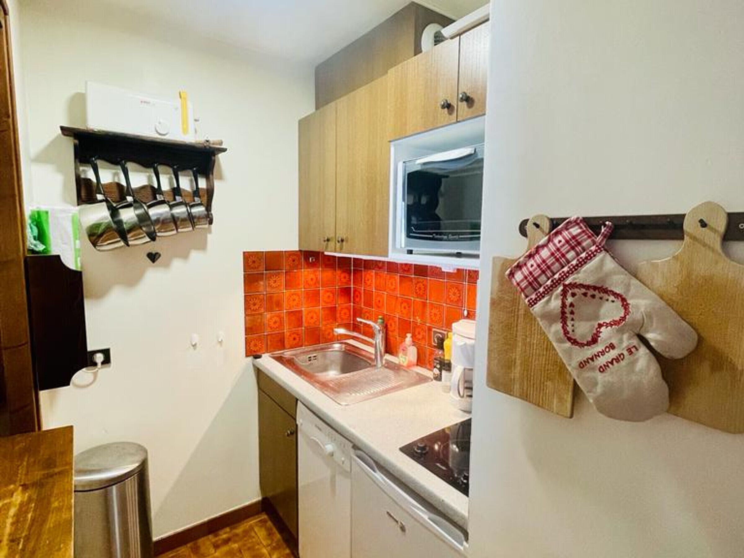 A compact kitchen with a dishwasher, a window, and a tiled backsplash.
