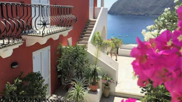 Un edifici vermell amb un balcó davant d'una vista al mar.