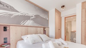 Ein Hotelzimmer mit einem großen Bett, Holzvertäfelung, einem Wandbild einer Berglandschaft und einem durchgehenden Türspalt erkennbaren Badezimmer.