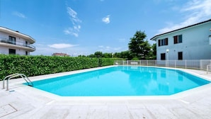 A rectangular swimming pool with a metal ladder on one side, surrounded by a white tiled deck.