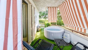 A balcony with a hot tub, artificial grass, and striped curtains.