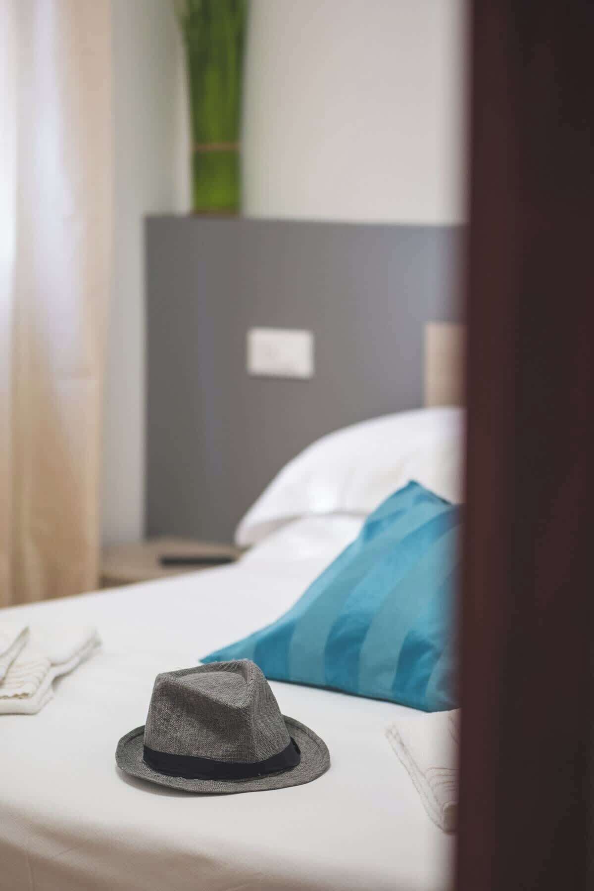 A neatly made bed with a grey hat, white pillow, and blue pillow.