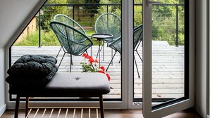 Una habitación con un banco de madera, una mesa pequeña y dos sillas verdes.
