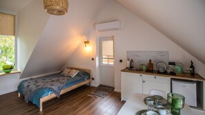 Un dormitorio tipo loft compacto y moderno con techo inclinado, una kitchenette pequeña y un área de comedor.