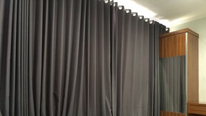 Een slaapkamer met een bed, een houten garderobe en een donker gordijn.