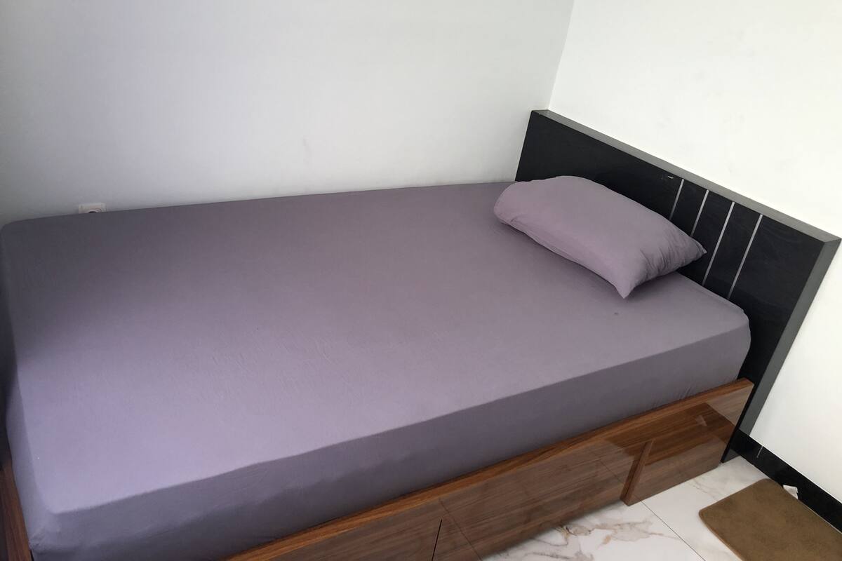 Una cama individual con estructura de madera y colchón gris.
