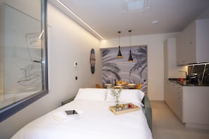 A modern hotel room with a bed, a dining area, and a kitchenette.