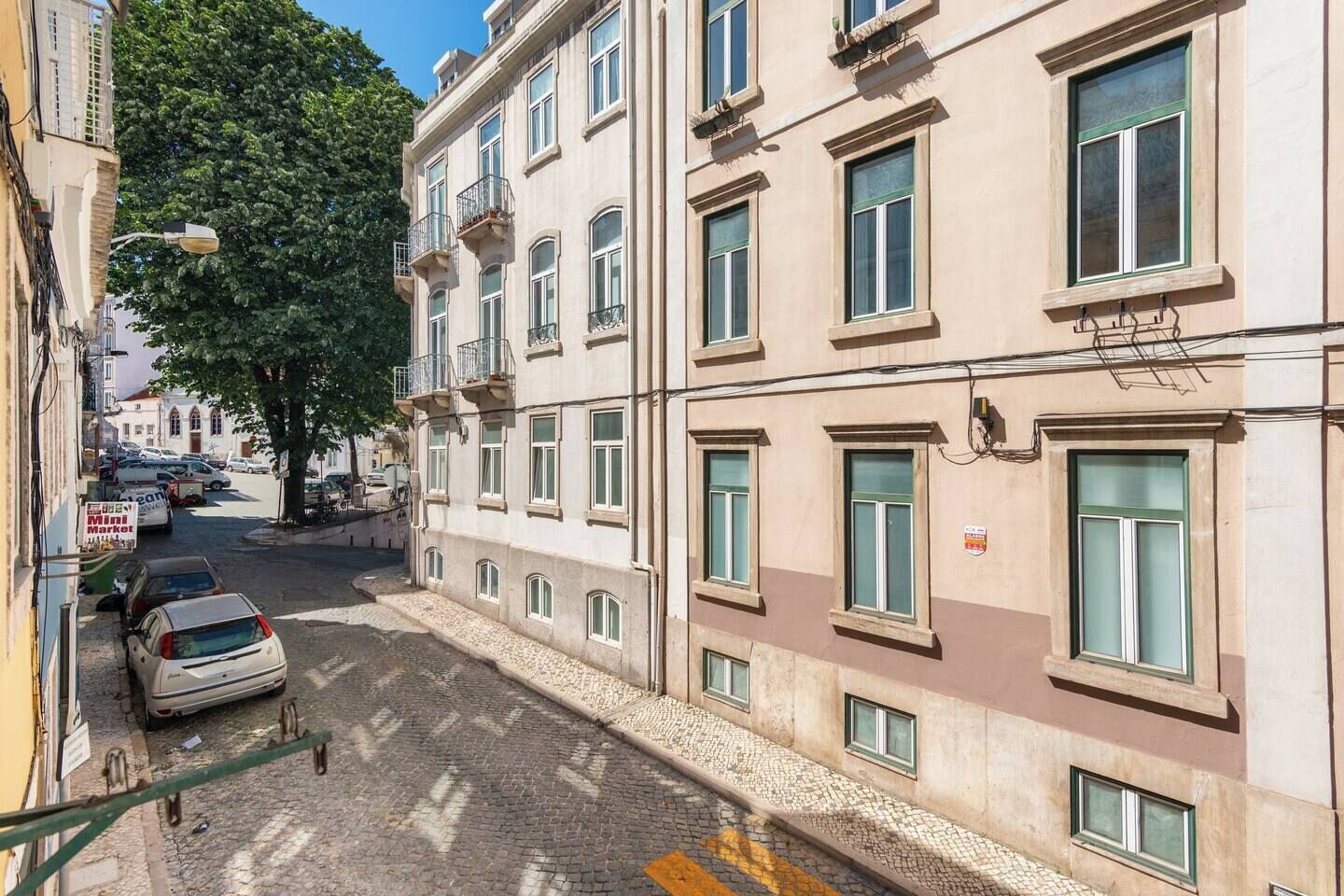 A narrow cobblestone street with a parked car and a building with multiple windows and balconies.