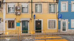 Un bâtiment avec une porte verte, un panneau de signalisation de stationnement bleu et une barrière jaune sur une rue pavée.