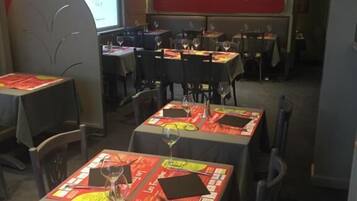 Een restaurant met gedekte tafels, een televisie aan de muur en een rode accentmuur.