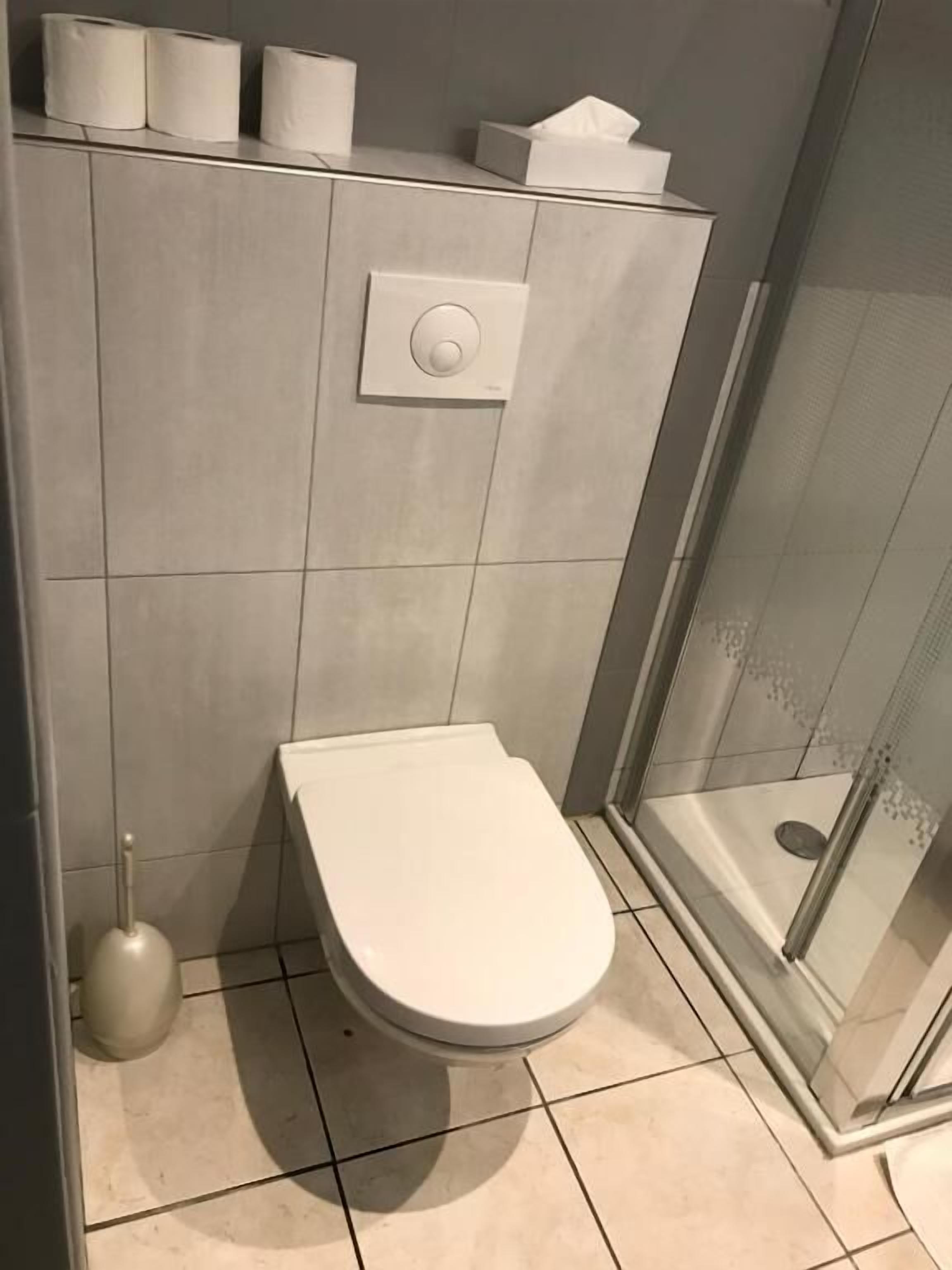 Ein modernes Badezimmer mit Toilette, Handtrockner und einer Duschkabine aus Glas.
