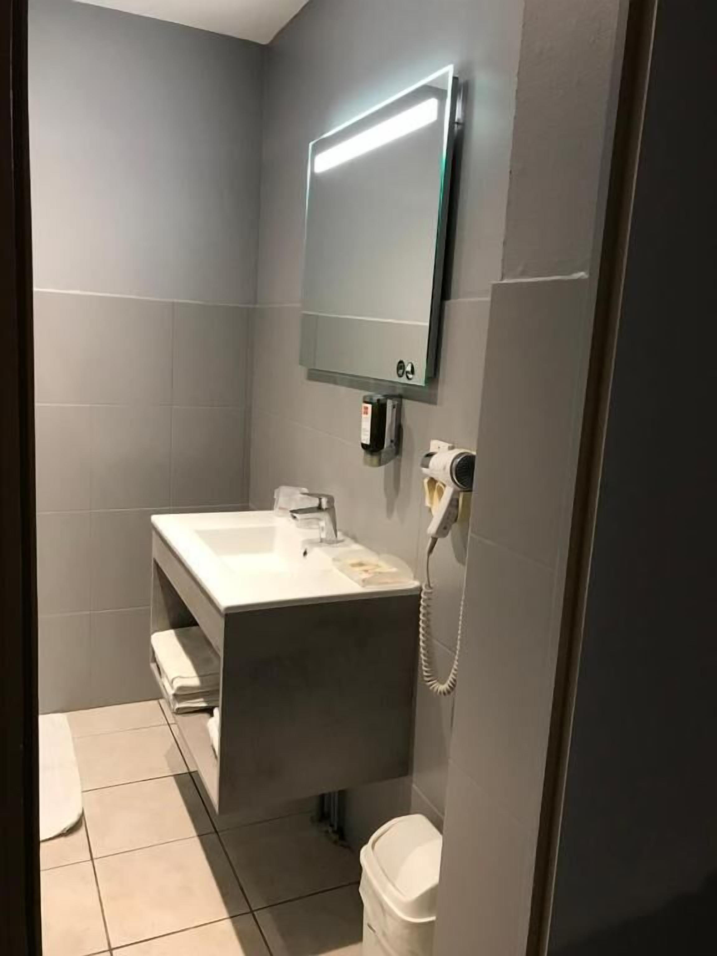 A modern bathroom with a large mirror, a white sink, and a toilet.