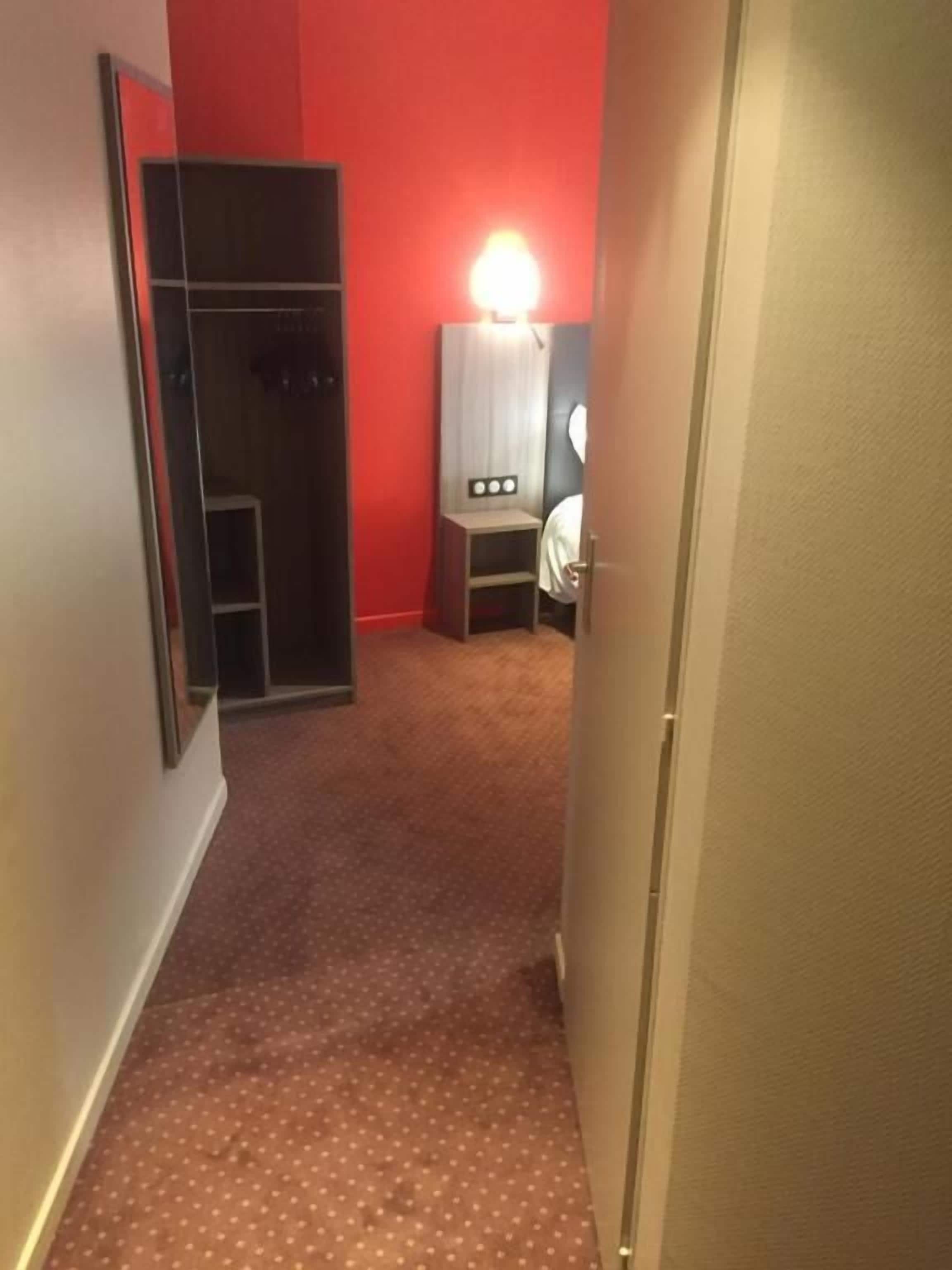 Un couloir étroit avec un mur rouge, un plancher en bois et un miroir sur le côté gauche.