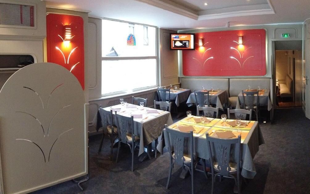 Un restaurante con mesas dispuestas para comer, un televisor montado en la pared y un ventanal que proporciona luz natural.