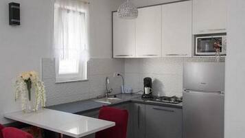 A compact kitchen with white cabinets, a stainless steel refrigerator, and a dining area with red chairs.