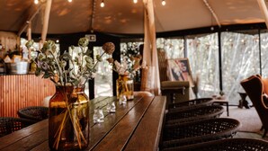 A rustic wooden table with glass vases containing dried flowers, under a tent with string lights. - The Lakes By YOO (Lechlade)