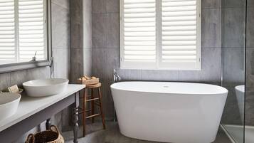 Un baño moderno con una bañera independiente, un lavamanos amplio y una ventana con persianas.