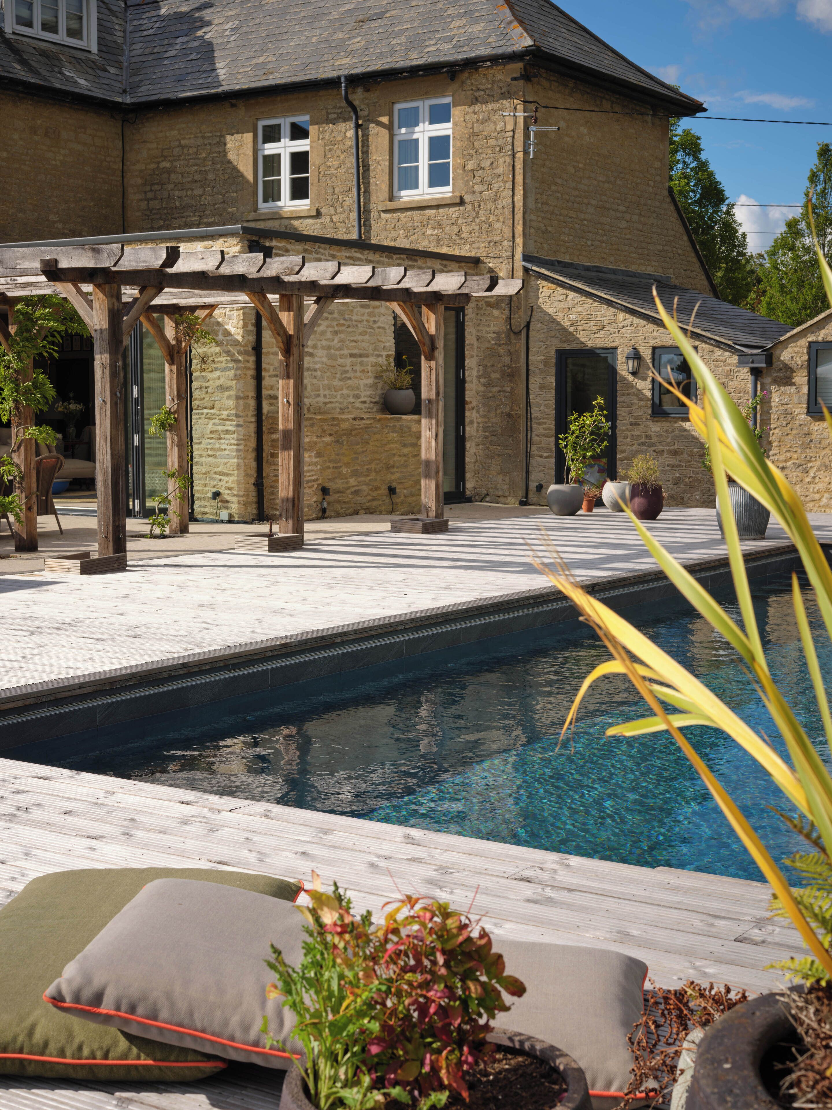 Una casa de piedra con piscina, pérgola de madera y mobiliario para exteriores.