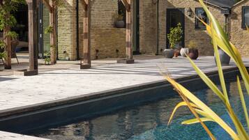 Una casa de piedra con piscina, pérgola de madera y mobiliario para exteriores.