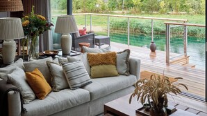 A modern living room with a sofa, lamps, and a view of a garden and water feature. - The Lakes By YOO (Lechlade)