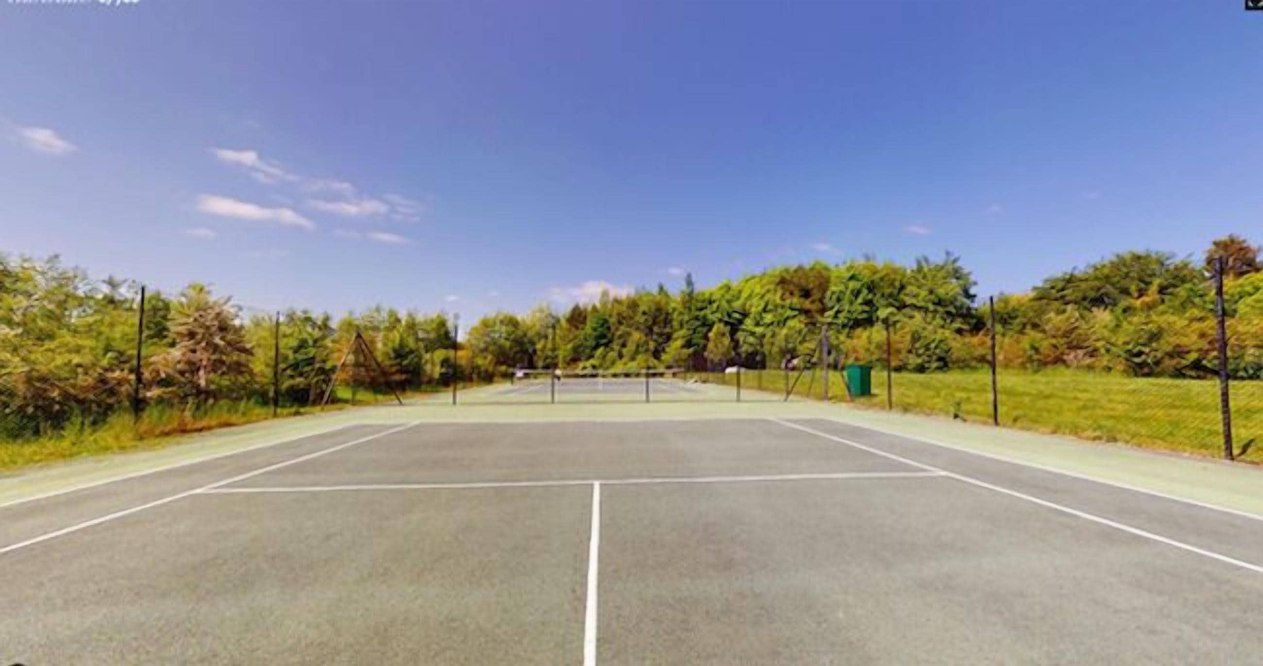 Una cancha de tenis al aire libre con una red, rodeada de árboles y un cielo despejado.