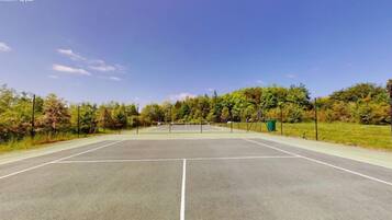 Una cancha de tenis al aire libre con una red, rodeada de árboles y un cielo despejado.