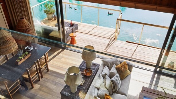 A modern interior with a wooden deck overlooking a pool and water. - The Lakes By YOO (Lechlade)