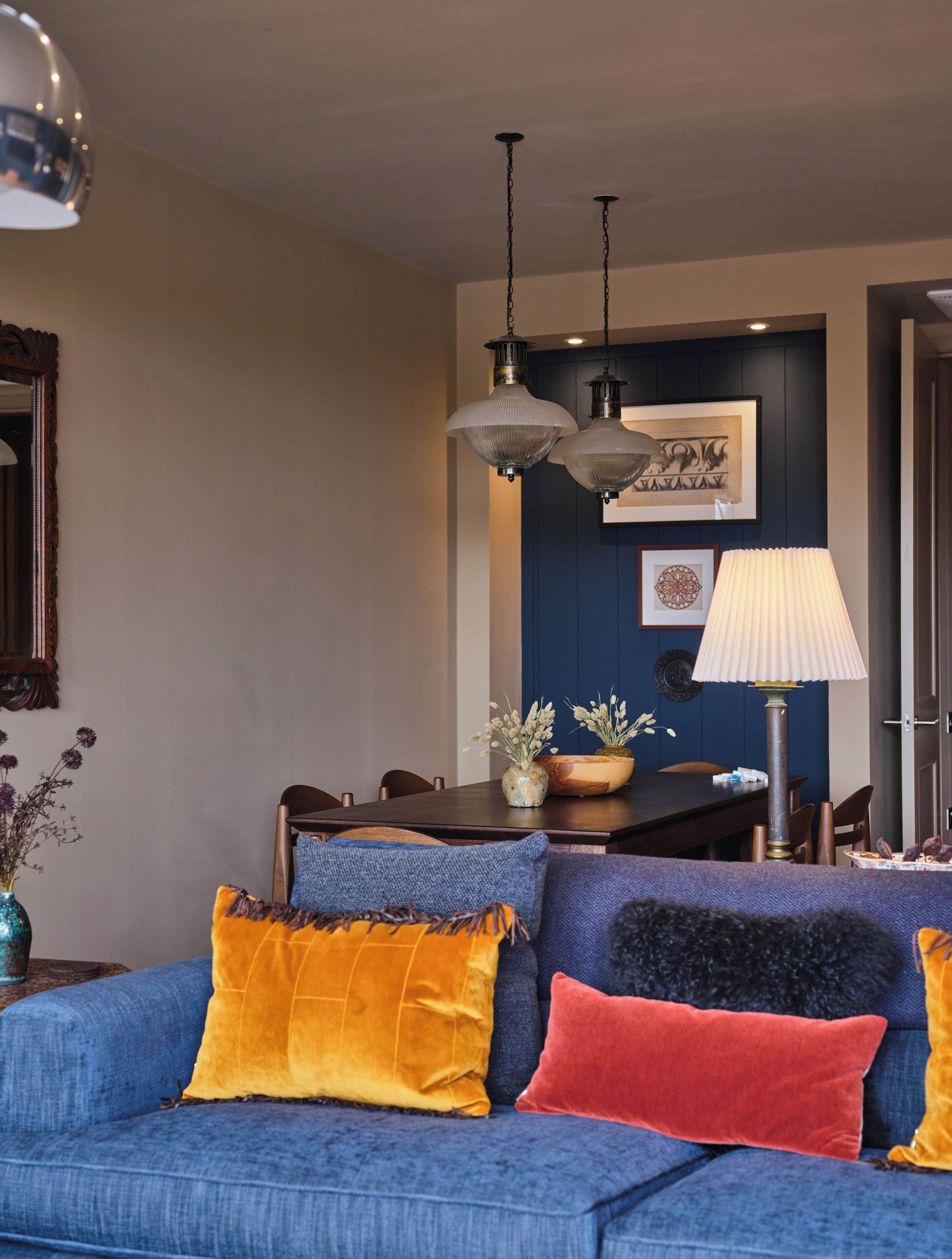 Una sala de estar moderna con un sofá azul, almohadones decorativos, una mesa de comedor y lámparas colgantes.