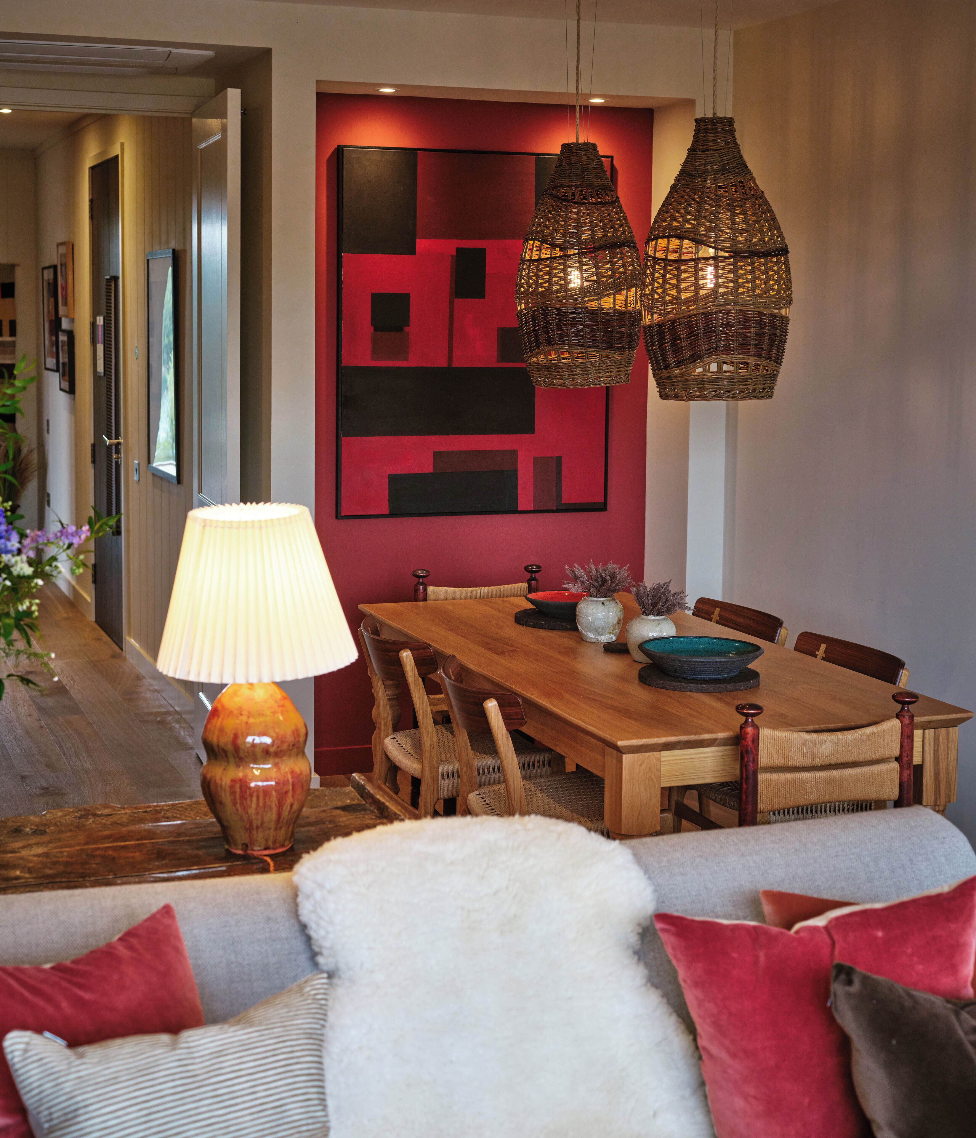 A dining area with a wooden table, wicker hanging lamps, and a modern red wall art piece.