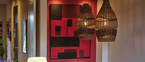 A dining area with a wooden table, wicker hanging lamps, and a modern red wall art piece.