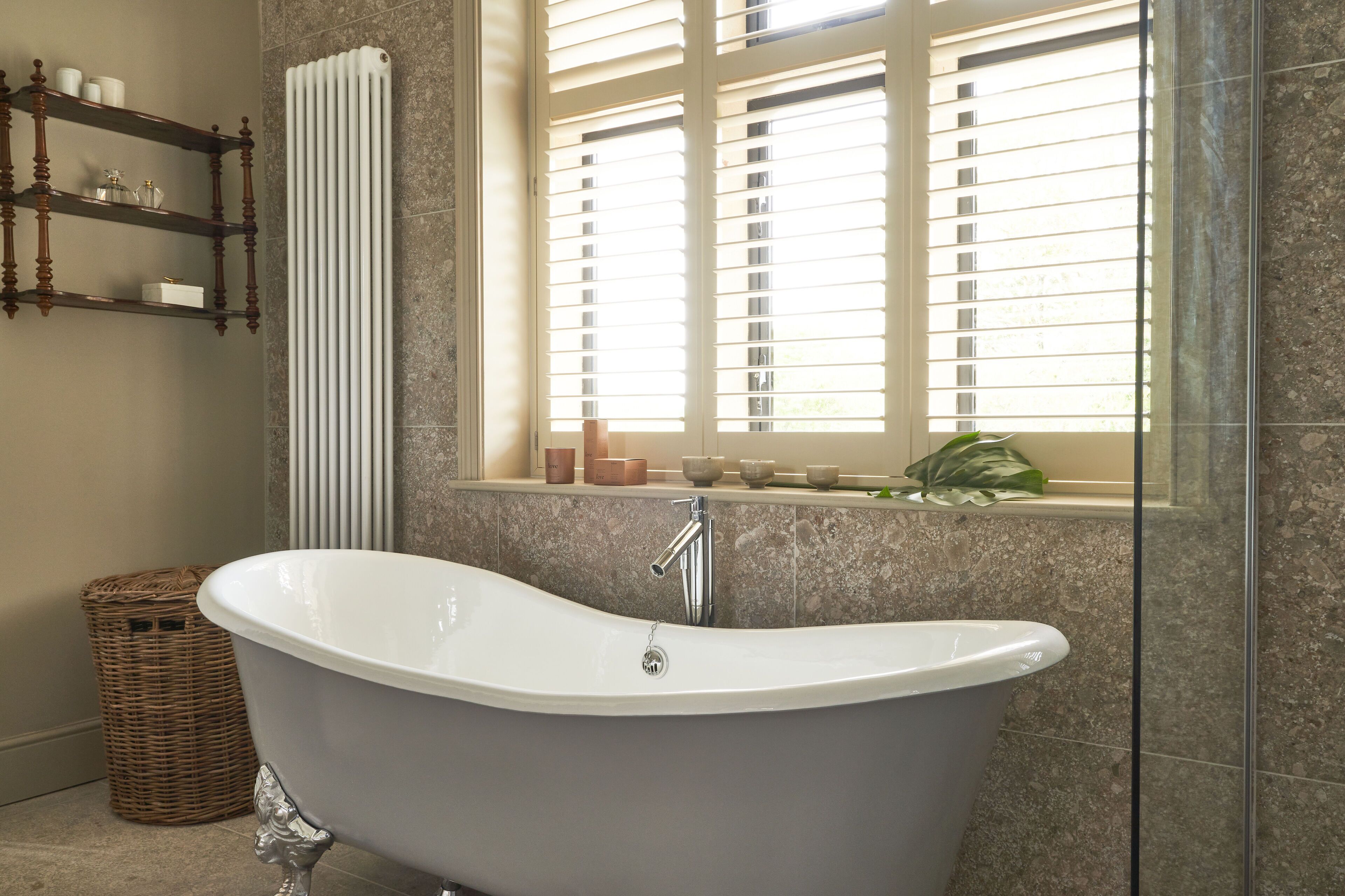 A bathroom with a freestanding bathtub, a wicker basket, and a window with blinds.