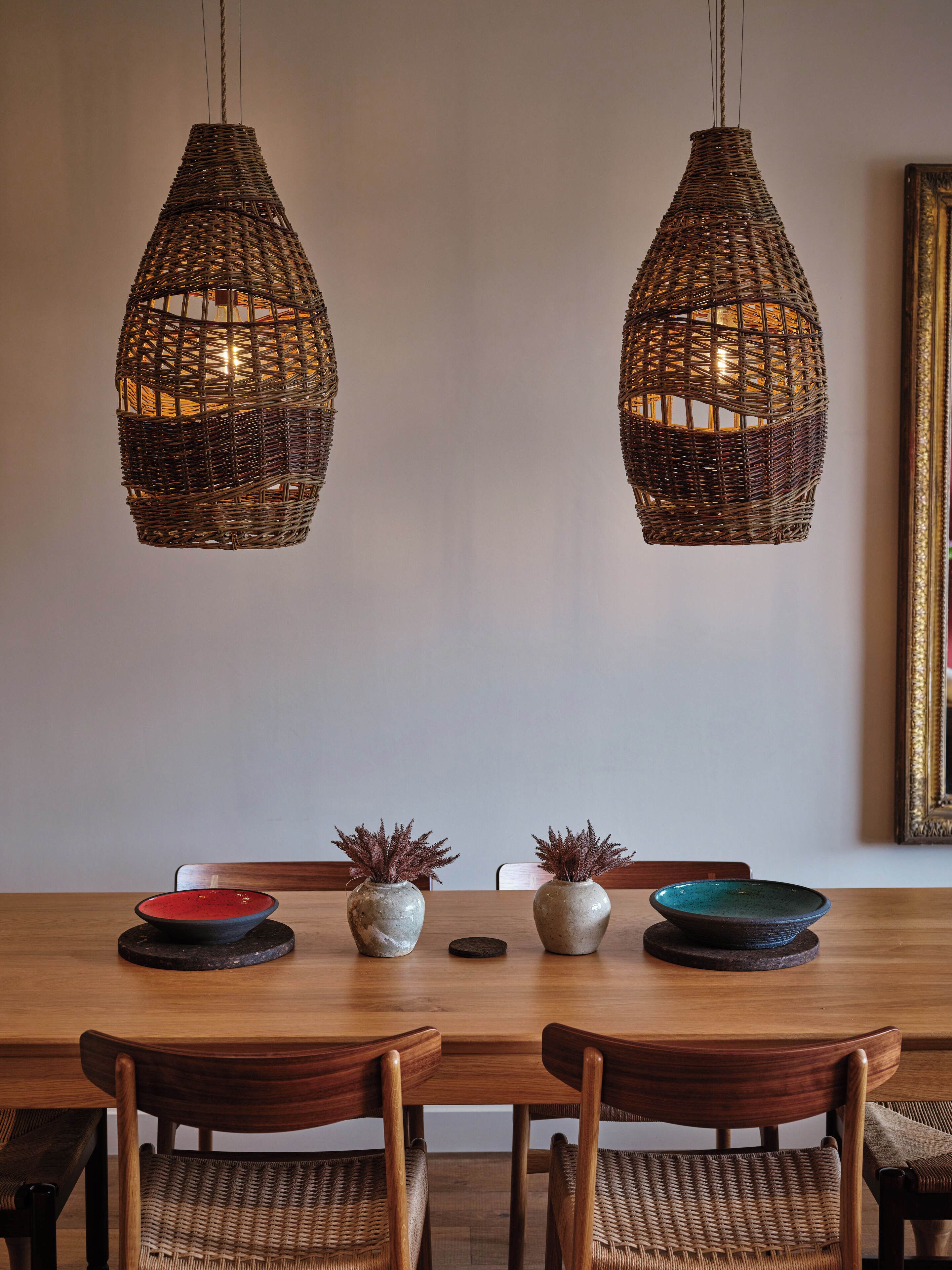 A dining area with a wooden table, two wicker pendant lights, and two ceramic vases with plants.