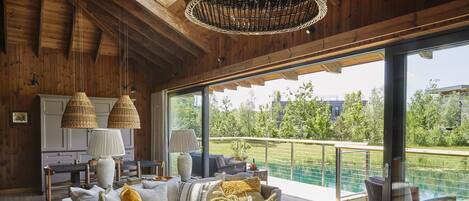 A modern living room with a large window, a wooden ceiling, and a dining area with a table and chairs.