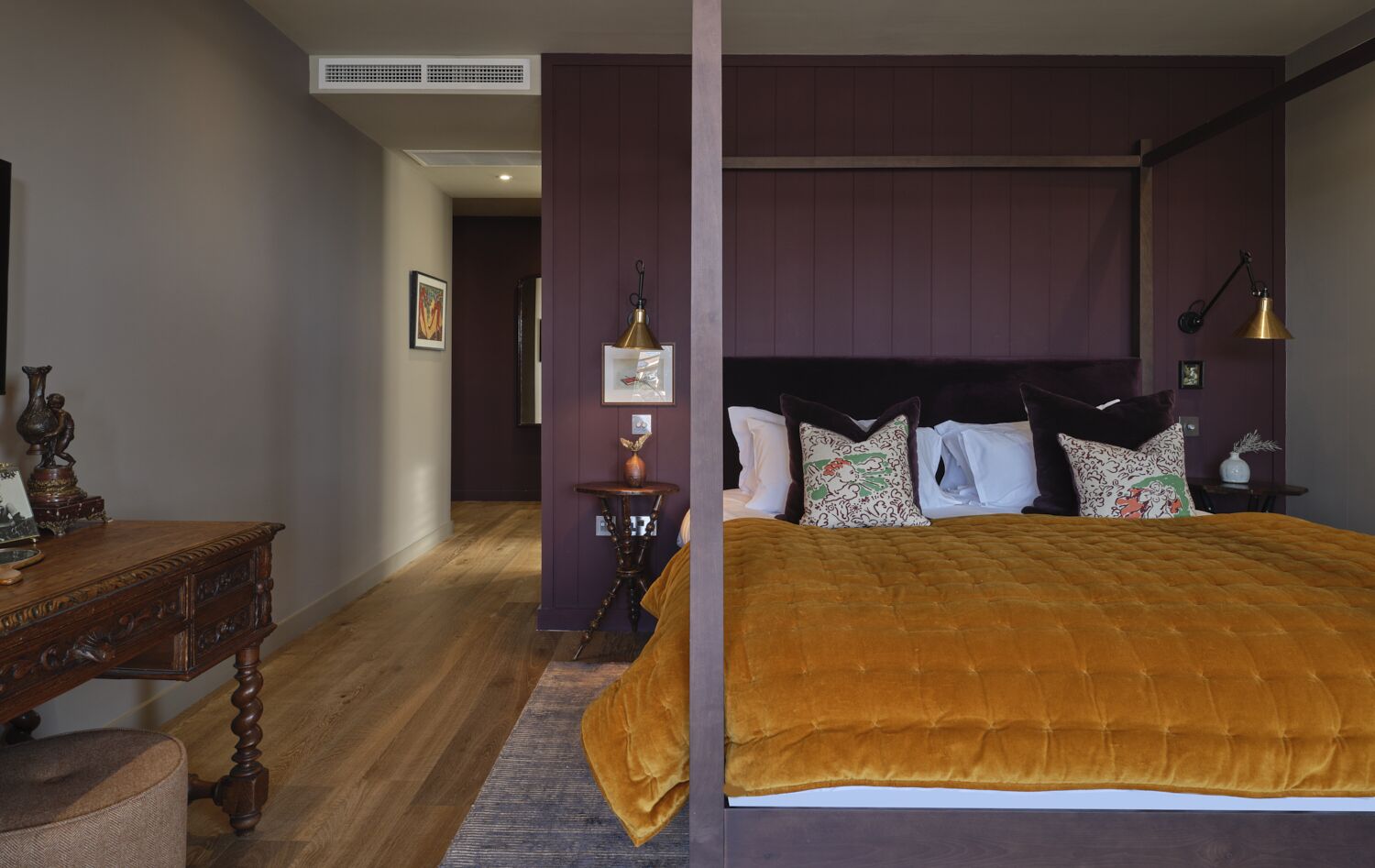 A bedroom with a large bed, a wooden nightstand, a desk, and a small table with a vase.