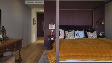A bedroom with a large bed, a wooden nightstand, a desk, and a small table with a vase.