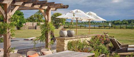 A wooden pergola with outdoor seating, including a table and chairs, surrounded by potted plants and umbrellas.