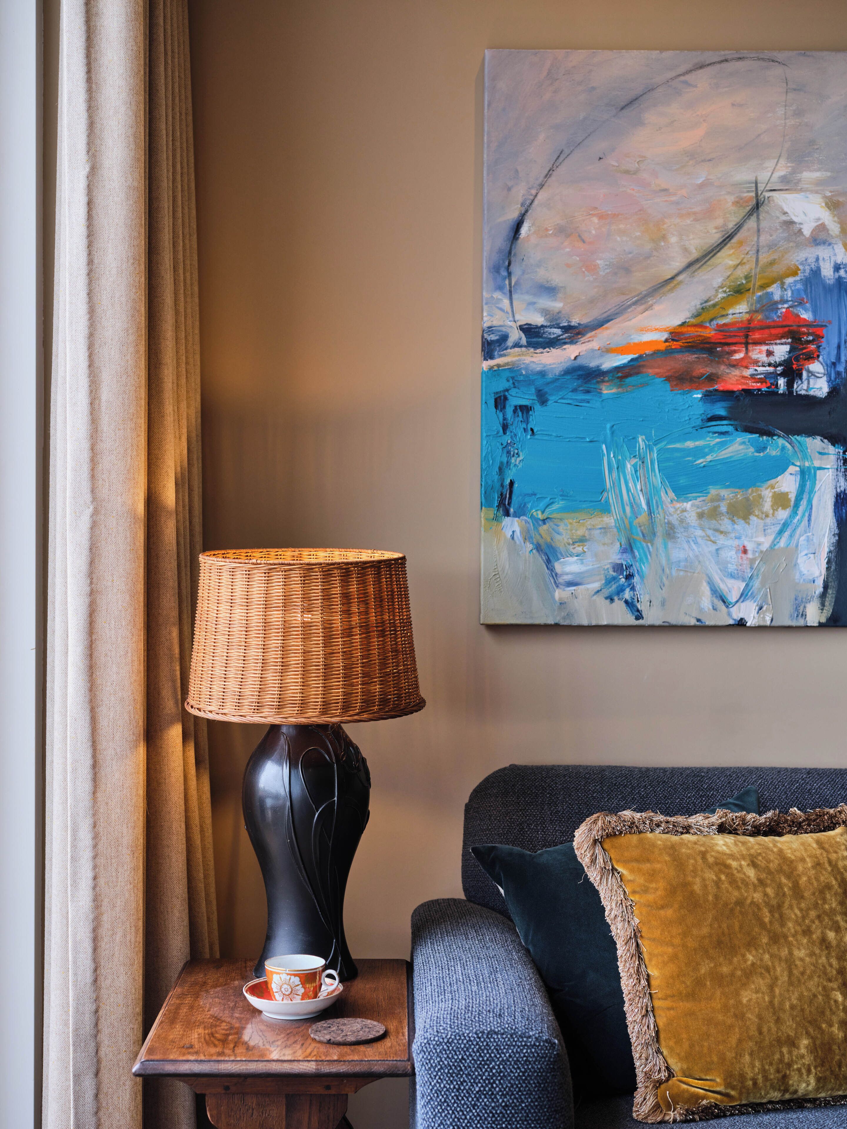 A room with a lamp, a painting, a sofa, and a table with a cup and saucer.