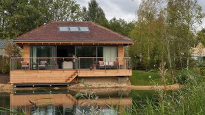 A house with a deck overlooking a pond, large windows, and a small staircase leading to the deck. - The Lakes By YOO (Lechlade)