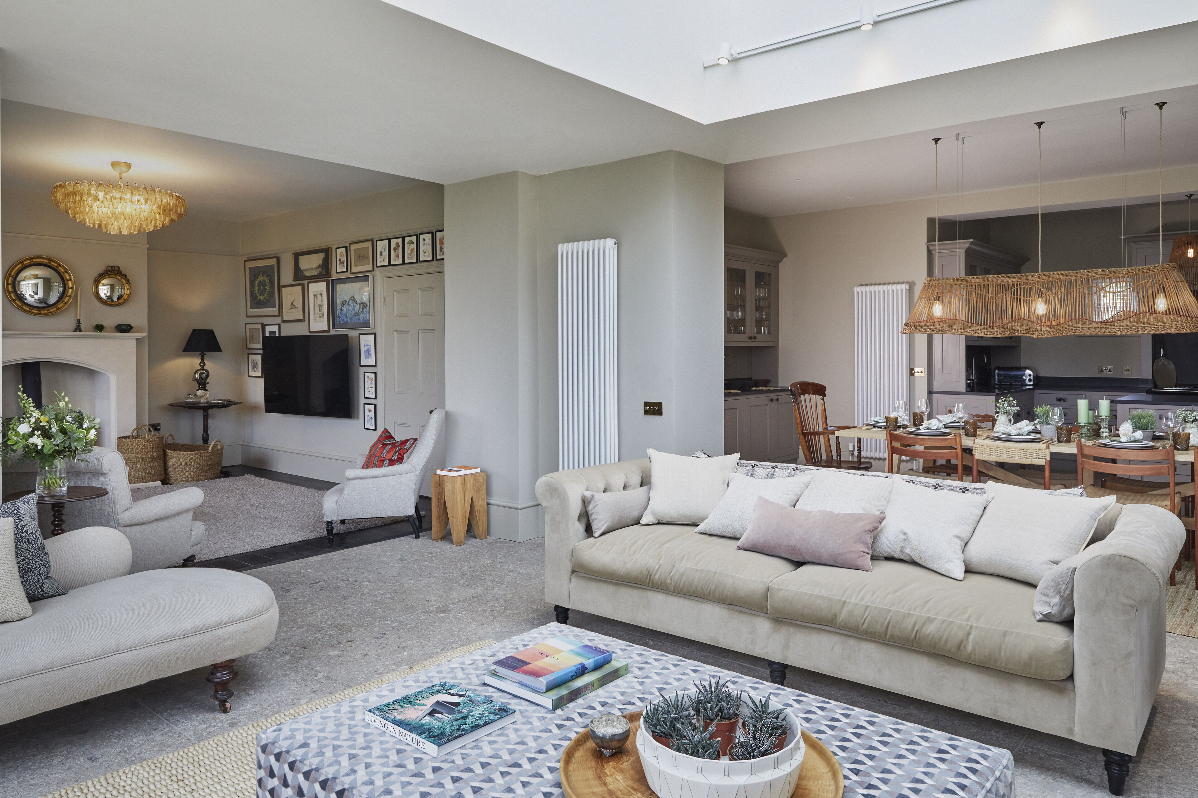 A spacious living room with a sofa, armchairs, and a coffee table. There is a fireplace, a television, and a dining area visible.